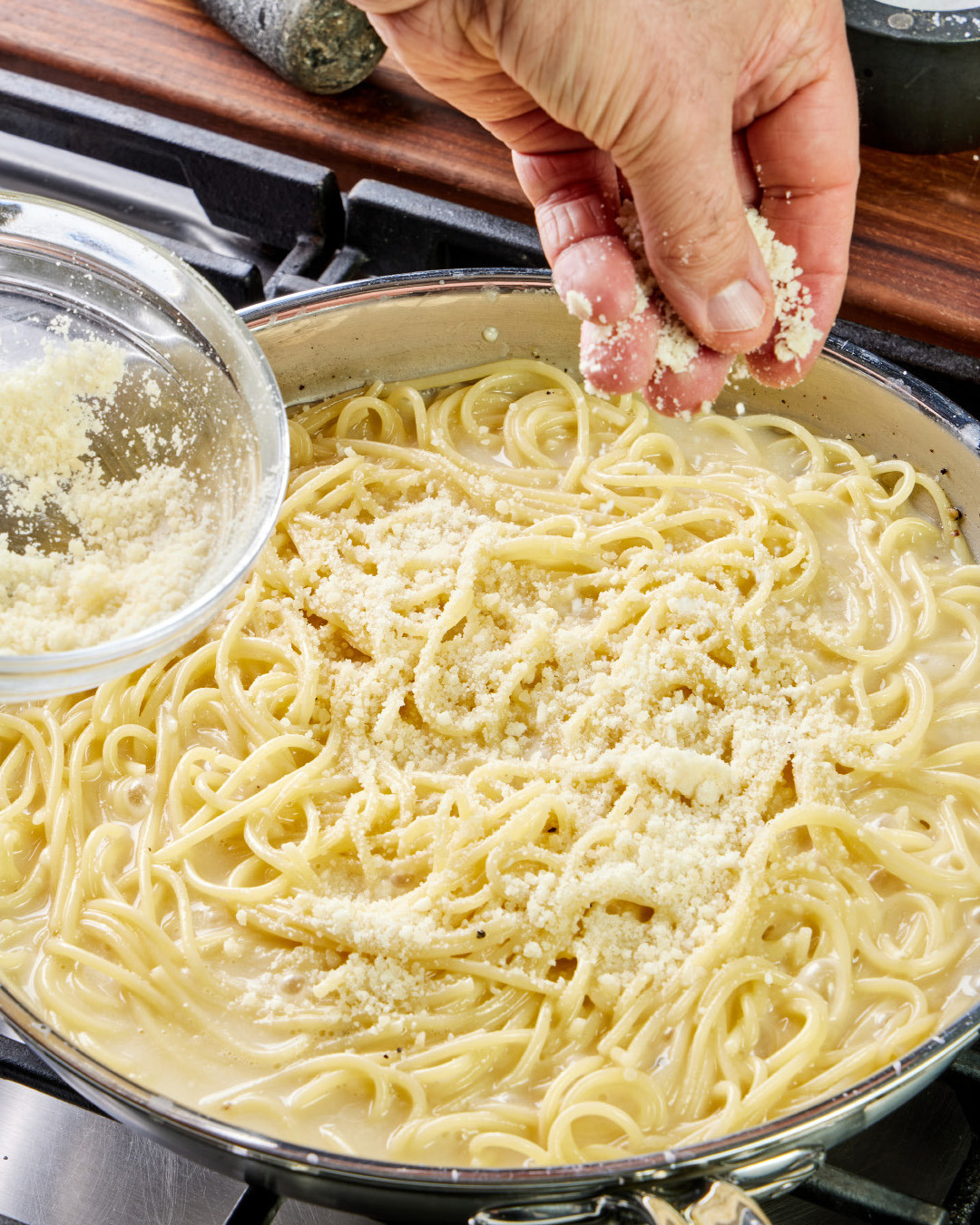 6. Add the remaining cheese mixture in two more additions, tossing until melted after each. The liquid will have formed a thin sauce that pools in the pan.
