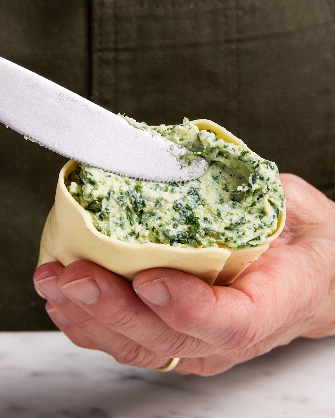 4. Holding the roll in one hand, use a butter knife or offset spatula to smooth any filling that is spilling out, gently pressing it back into the rolled pasta.