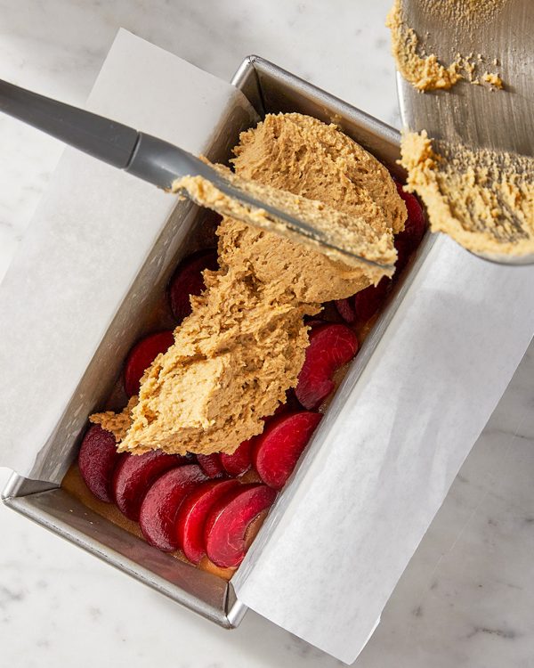 Plum cake batter scraped into loaf pan over fruit and caramel